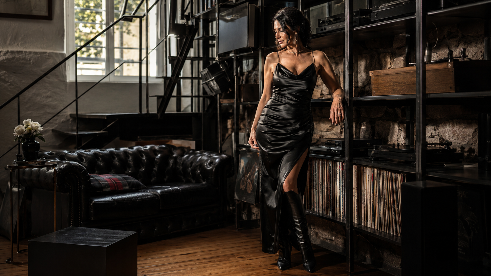 Stehendes Model im glänzenden schwarzen Kleid zwischen Sofa und Stahlregal